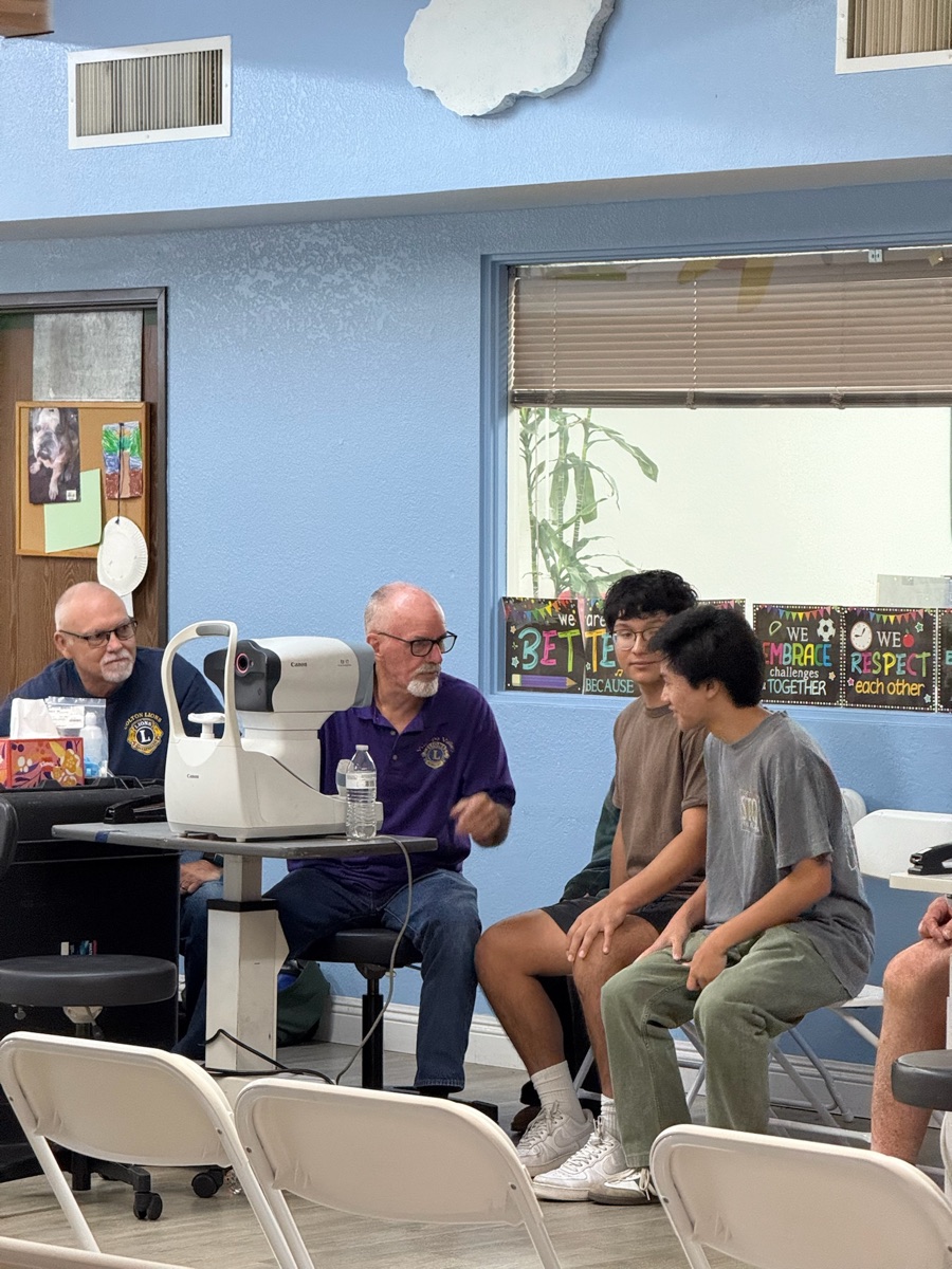 Isaac and Dylan observing vision screening equipment with Lions Club volunteers